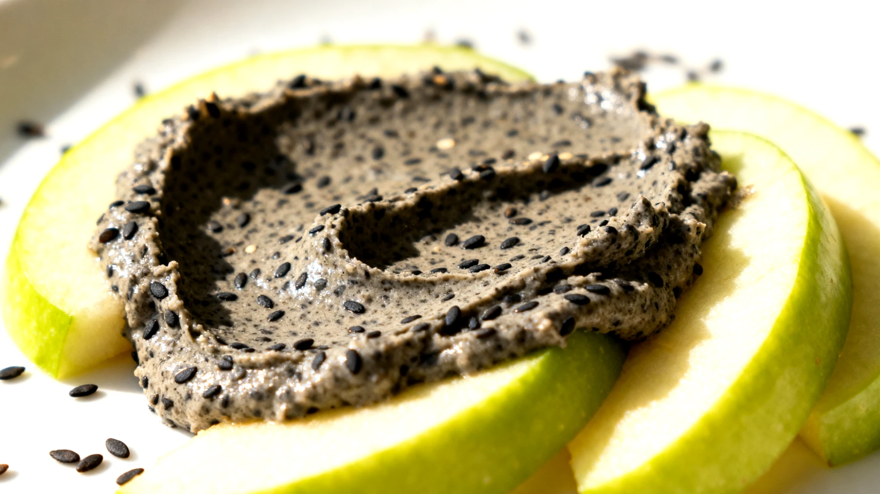Crema di sesamo nero (tahini nero) spalmata su fette di mela verde"